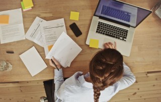 woman seen from top with paperwork and using laptop