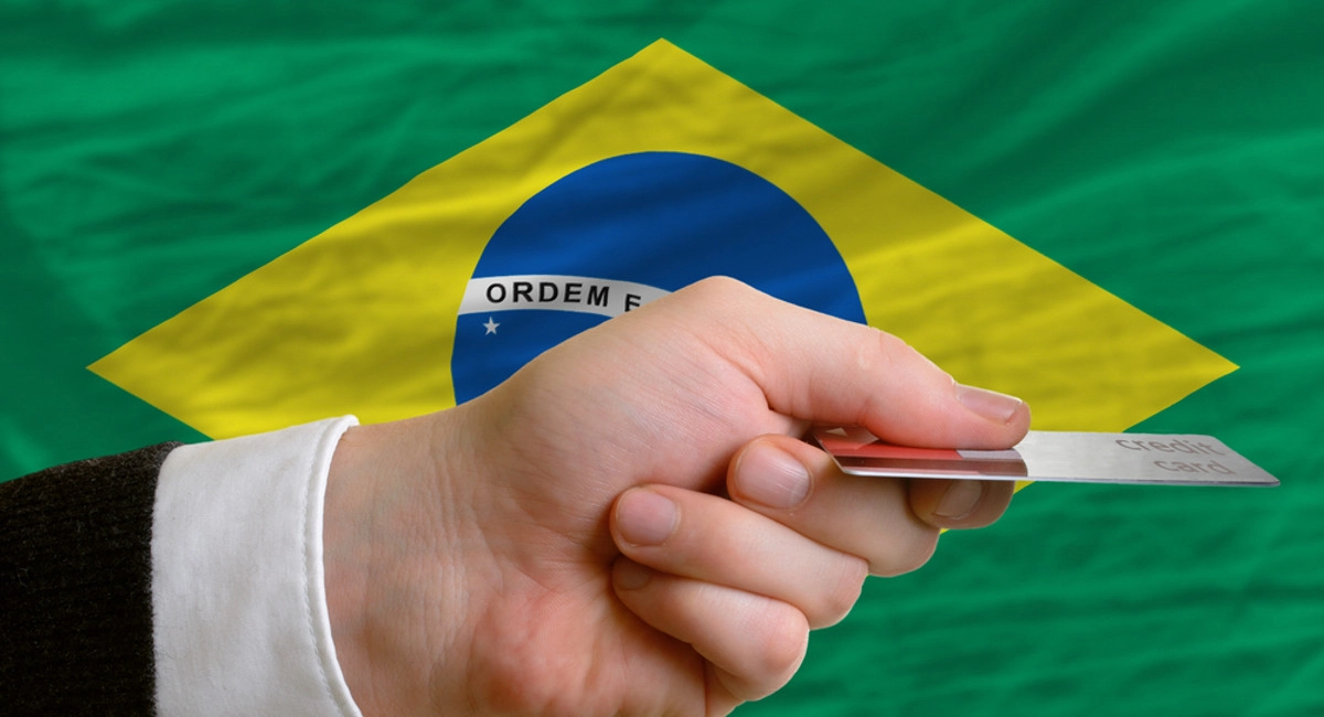 hand with credit card in front of Brazilian flag