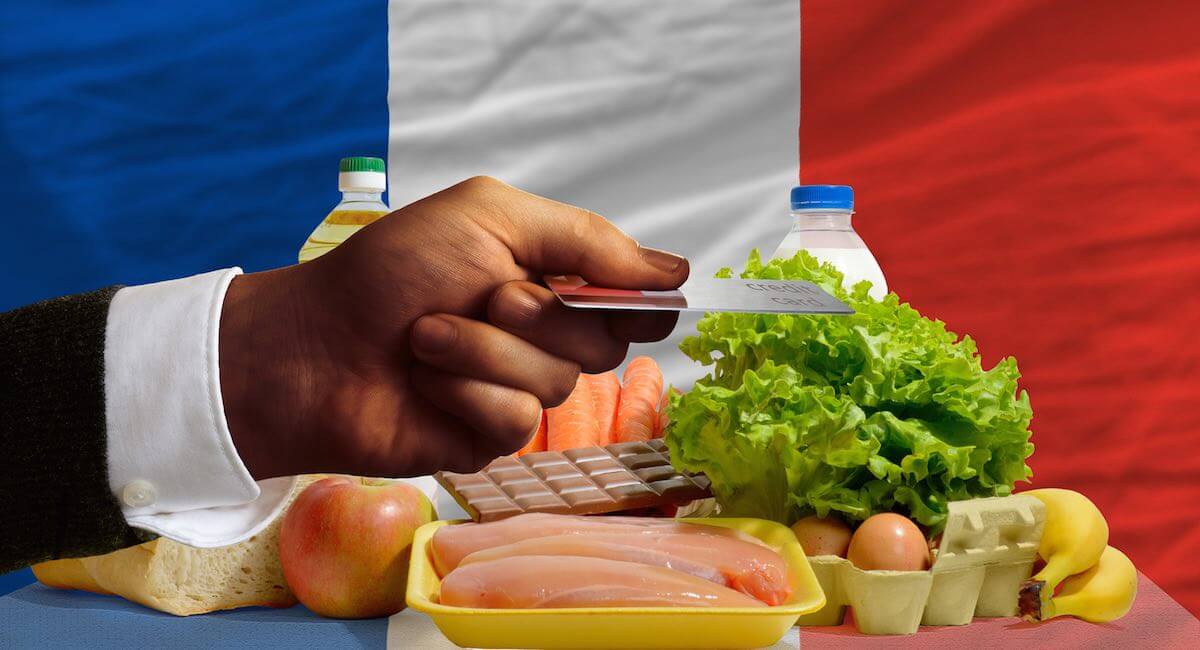 hand holding credit card in front of French flag and selection of food